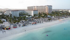 Un resort con diversi edifici, una spiaggia con ombrelloni e una vista libera sull'oceano.