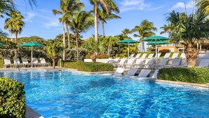 Una piscina con lettini e ombrelloni, immersa nel verde e circondata da palme.