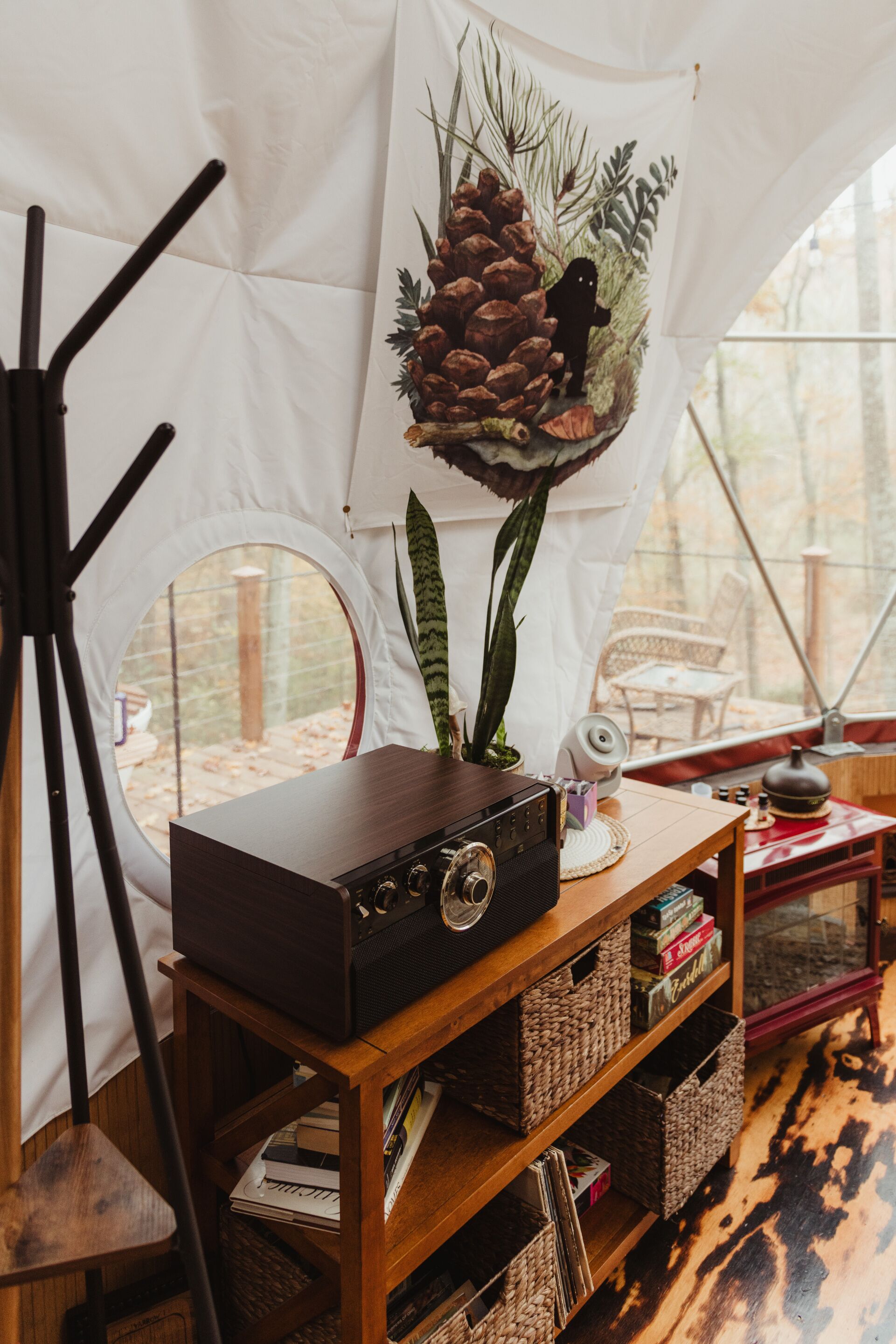 Interior de una carpa con una radio antigua, estanterías, un trípode para cámara y una decoración de piñas.