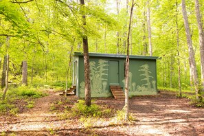 Een groene houten hut met een hellingbaan en een deur, omringd door bomen in een bos.