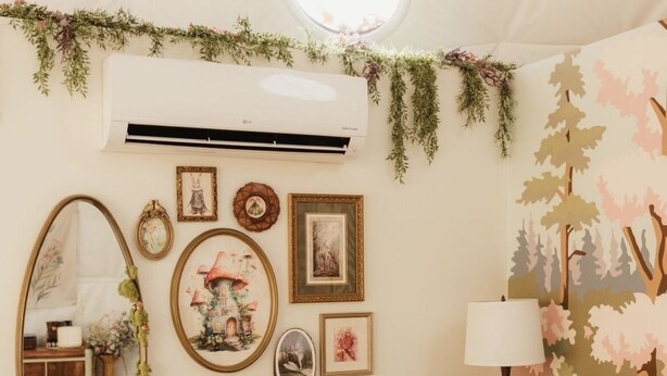 Een slaapkamer met een bed, een spiegel aan de muur, een lamp en een wand versierd met ingelijste foto's en een guirlande.