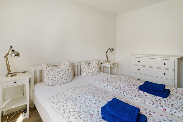 A bedroom with two beds, a bedside table with lamps, a dresser, and a white radiator.
