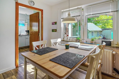 A dining area with a wooden table, black placemats, white chairs, a hanging pendant light, and a view of a garden through a window.. Holiday Home 'Ferienhaus Mecki' with Private Terrace, Private Garden and Wi-Fi
