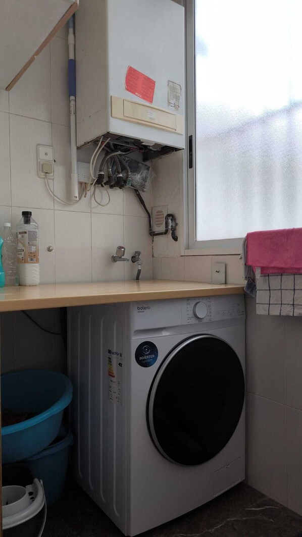 A compact laundry room with a washing machine, a sink, and a window.