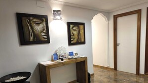 A hallway with a wooden console table, two framed artworks, a wall-mounted light fixture, and a closed door.