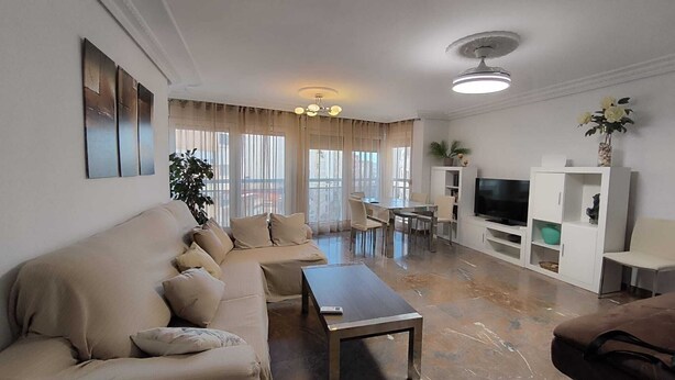 A living room with a sofa, a coffee table, a TV stand, and a dining area with a table and chairs.