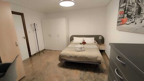 A neatly arranged bedroom with a bed, a bedside table, a lamp, a wardrobe, and a coat rack.