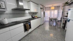 A kitchen with white cabinets, a black countertop, a stainless steel range hood, and a dining area with a table and chairs.