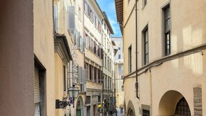 Una calle estrecha flanqueada por edificios, algunos peatones y un cielo despejado.