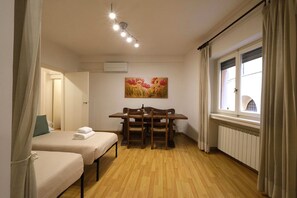 Una stanza con due letti, un tavolo di legno, una finestra con tende e un quadro appeso al muro.