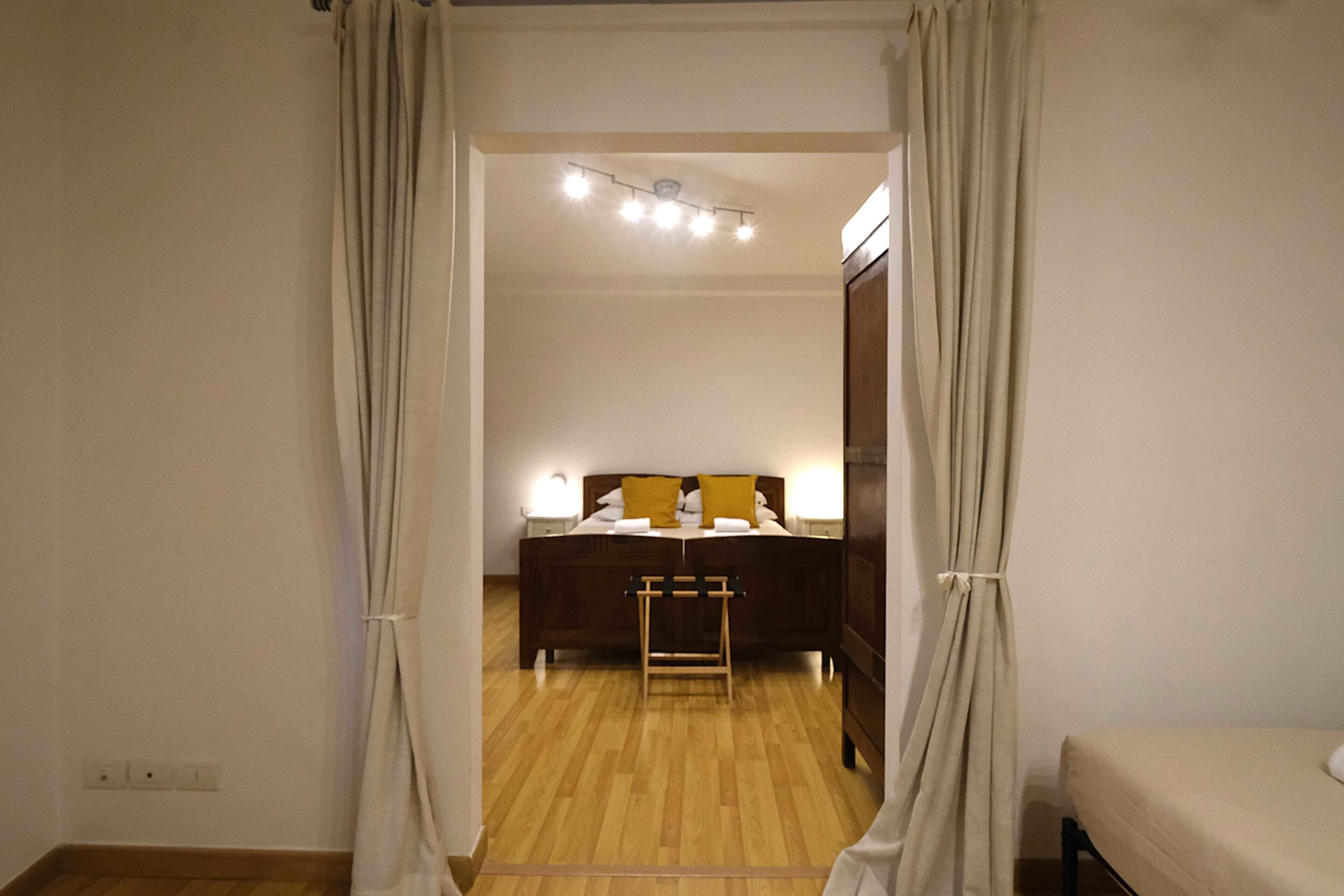 A bedroom with a wooden floor, a bed with a headboard, and a bedside table with a lamp.