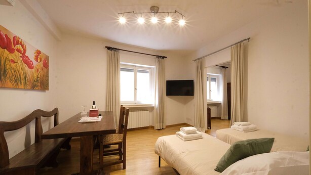 Una habitación con una mesa de comedor de madera, una cama individual con almohadas, un televisor y una ventana con cortinas.