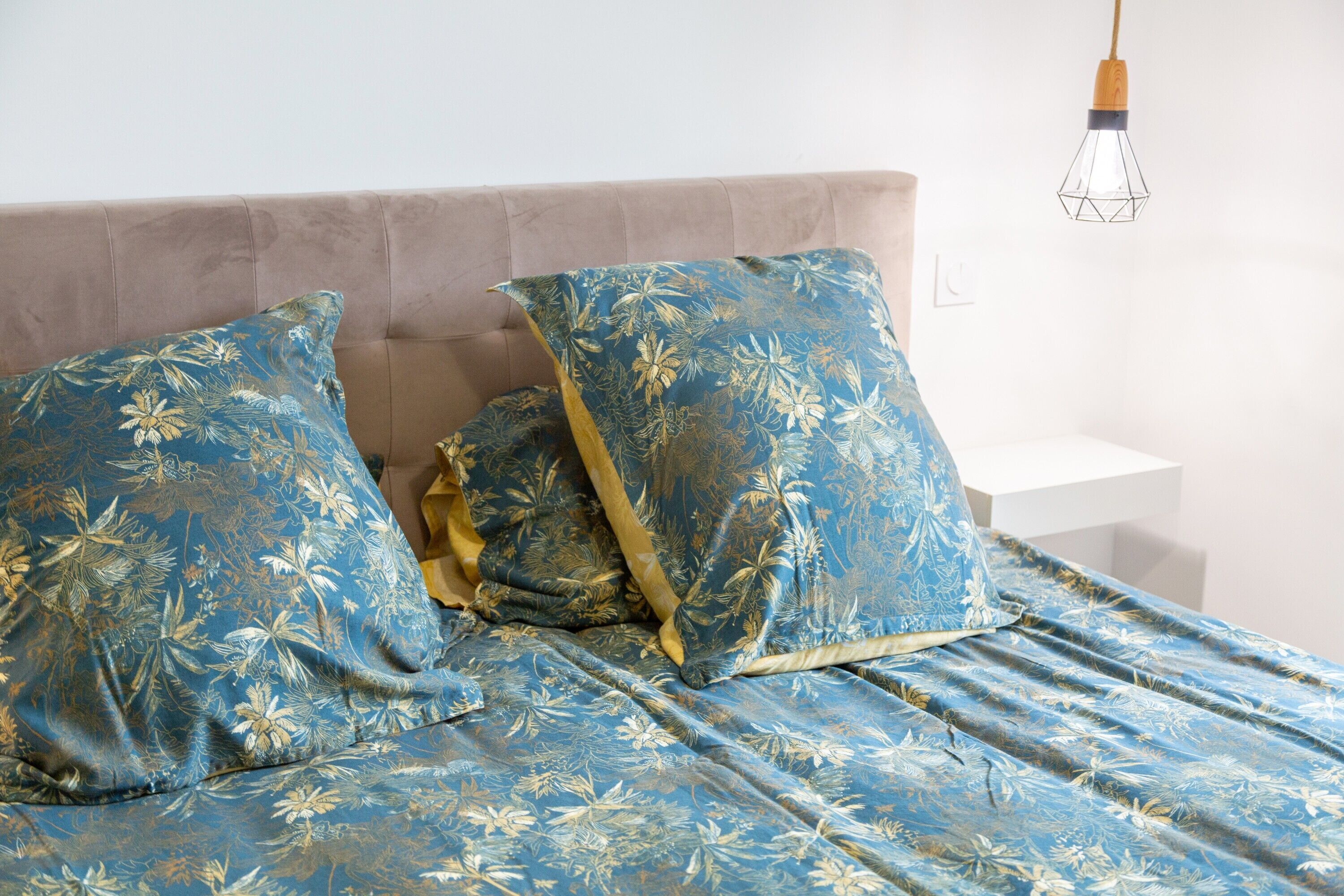 A bed with floral-patterned bedding, a headboard, and a hanging light fixture.