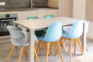 A modern kitchen with a wooden table and four chairs, a built-in oven, and a sink.