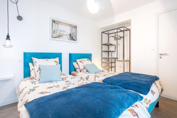 Een tweepersoonsbed met een blauw hoofdeinde en een kleurrijke sprei met een vissenmotief.