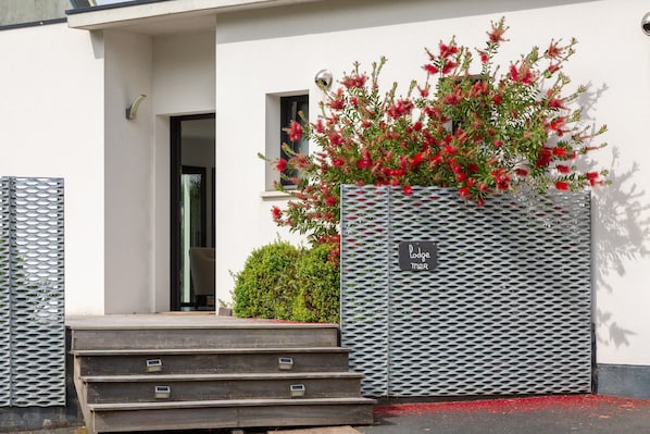 Un ingresso di un edificio con gradini che portano a una porta, una recinzione in metallo con un cartello e un cespuglio con fiori rossi.