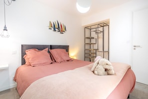 Une chambre à coucher avec un lit, des oreillers, une étagère fixée au mur et un luminaire suspendu.