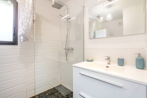A modern bathroom with a glass shower enclosure, a white vanity with a mirror, and a tiled floor.