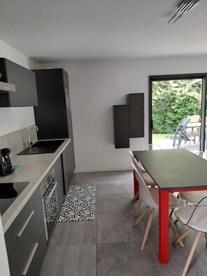 A modern kitchen with a built-in stove, a dining area with a table and chairs, and a view of a garden through a glass door.