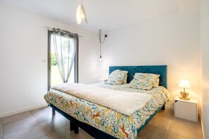 A bedroom with a bed, a nightstand, a lamp, a window with curtains, and a hanging light fixture.