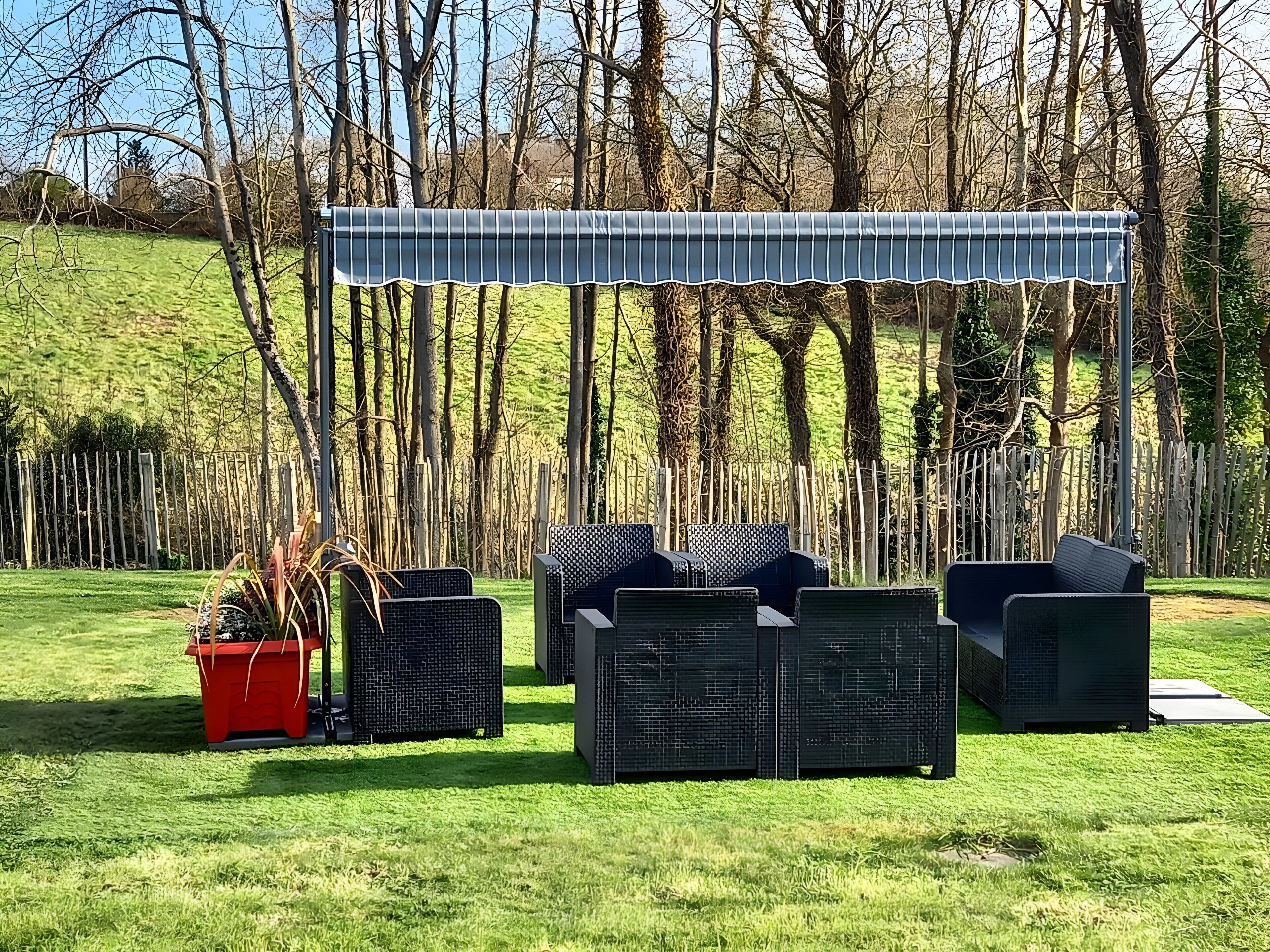 En utomhusplats med sittmöbler, en pergola, möbler av rotting och en röd blomkruka.