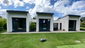 Une maison moderne à deux étages, dotée de grandes portes vitrées, d’une pelouse bien entretenue et d’une tondeuse à gazon visible au premier plan.