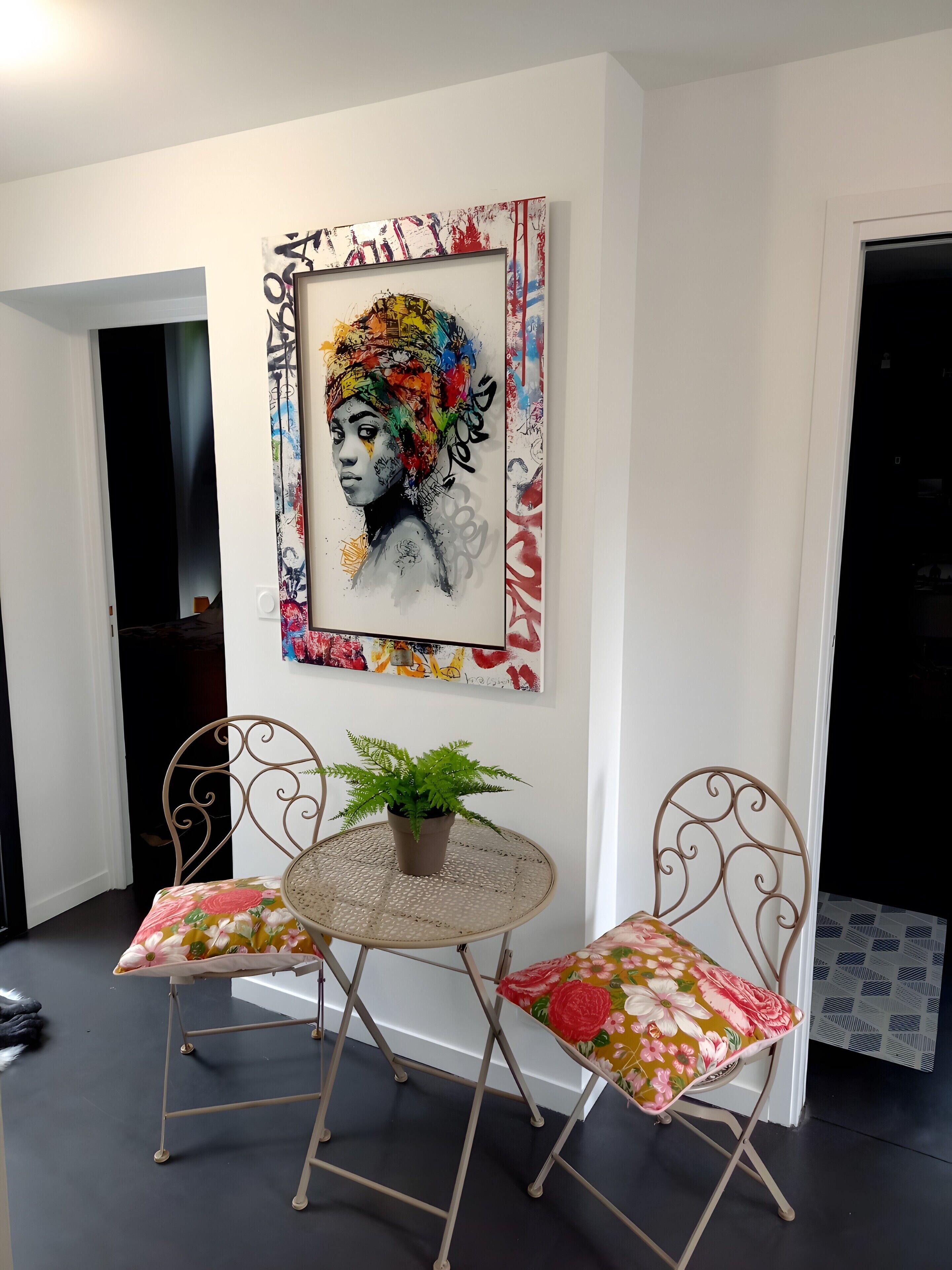 Un coin repas comprenant une table ronde, deux chaises, une plante en pot et une œuvre d’art accrochée au mur.