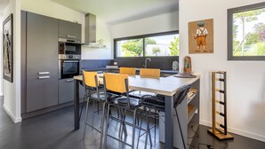 Une cuisine moderne avec des meubles gris, un four encastré et un coin repas comprenant une table et des chaises.