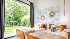 Une chambre avec deux lits, une grande fenêtre et une vue sur un jardin.