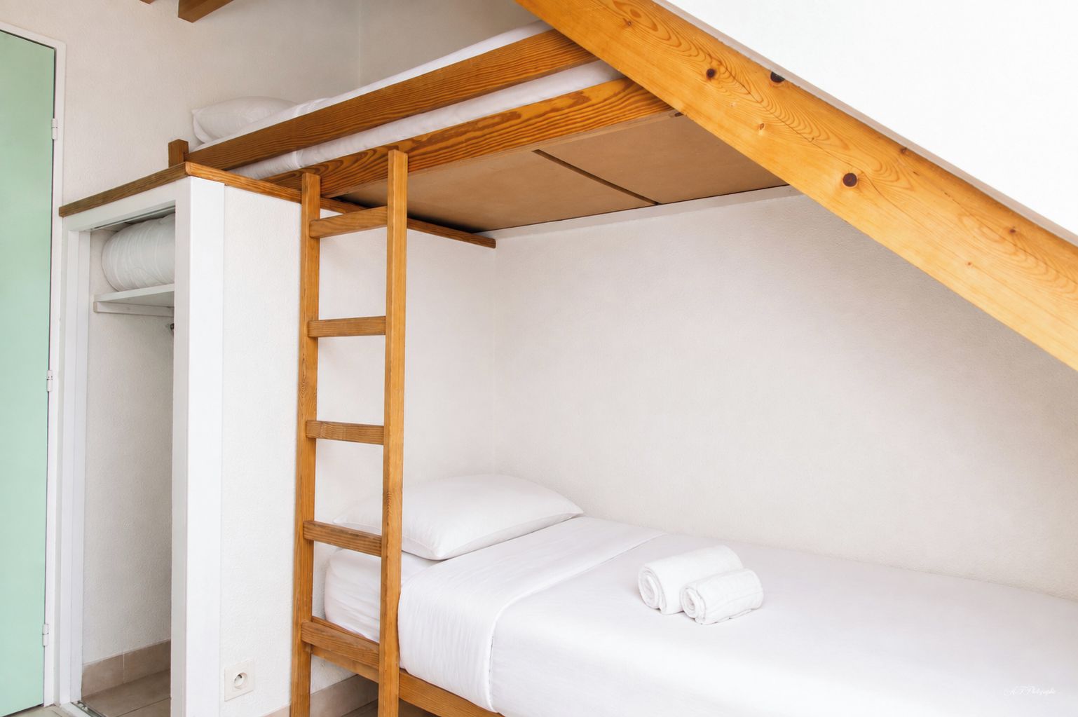 A bunk bed with a wooden ladder, white bedding, and a green door.