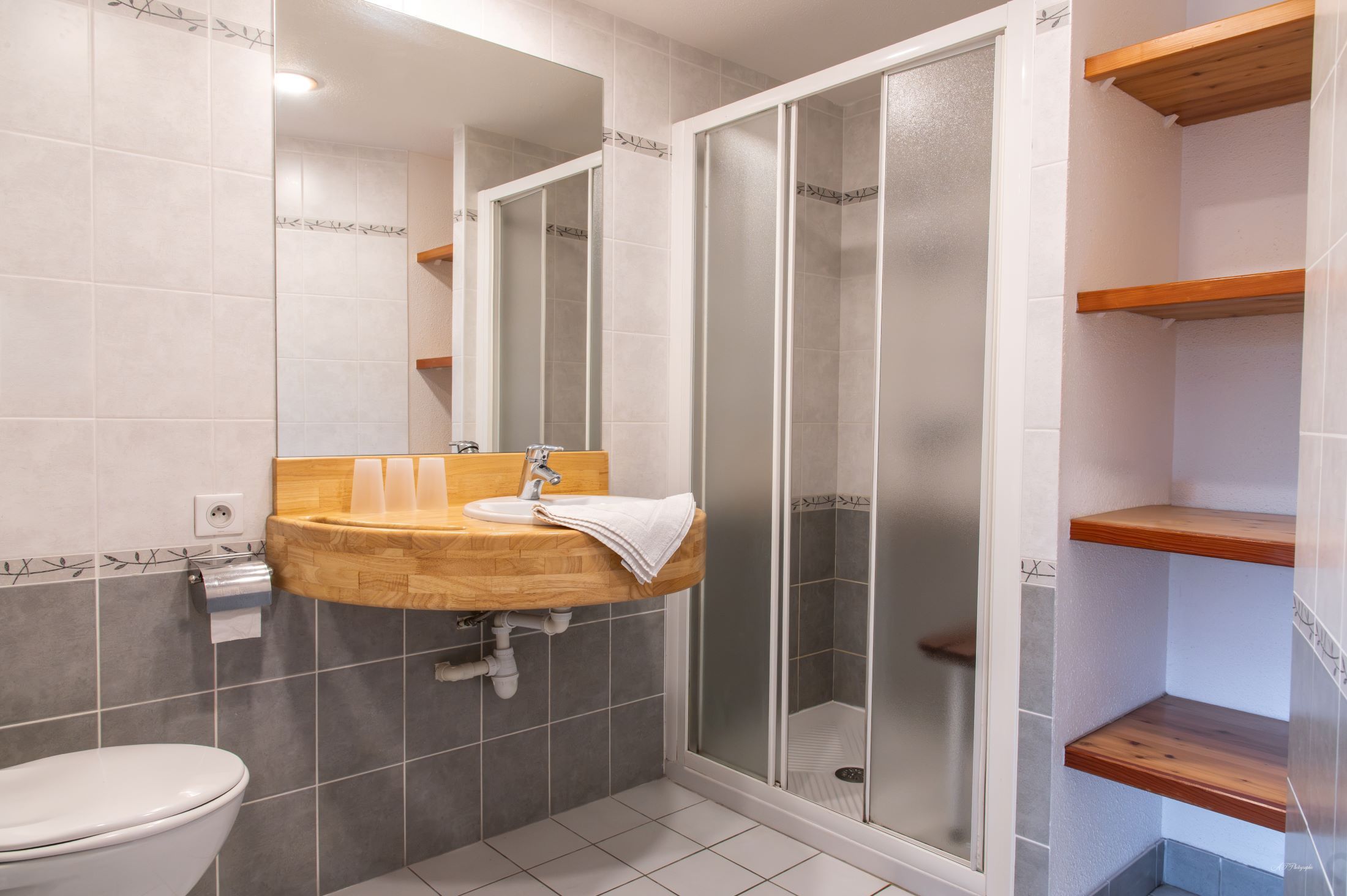 A bathroom with a wooden vanity, a toilet, and a glass-enclosed shower.