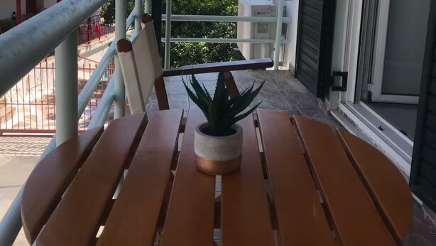 Una mesa de madera con una planta en maceta en un balcón con baranda metálica, con vistas a un paisaje montañoso.