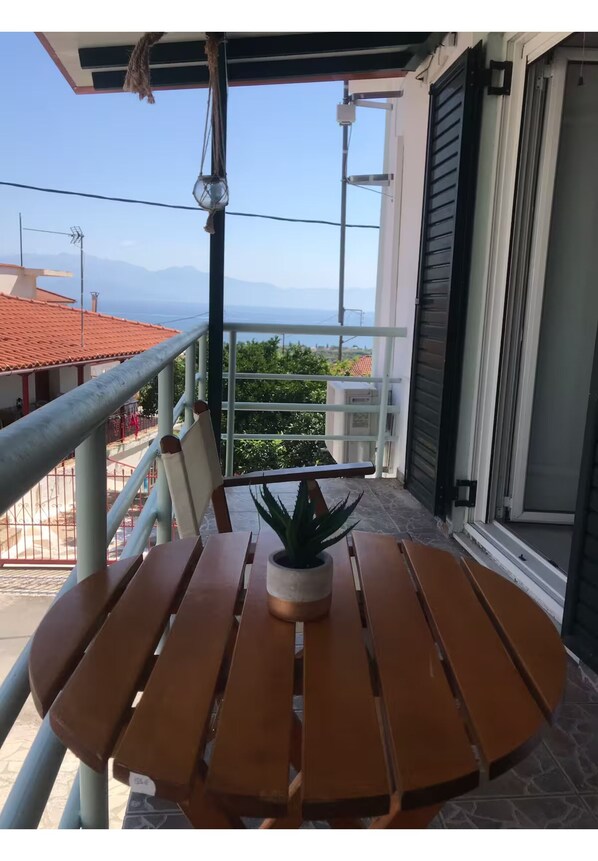 A wooden table with a potted plant on a balcony with a metal railing, overlooking a mountainous landscape.