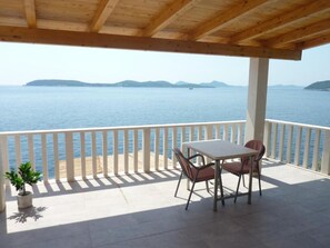 A covered outdoor area with a table and chairs, overlooking a body of water and distant landforms. - 2-bedroom apartment -sea view (Dubrovnik)