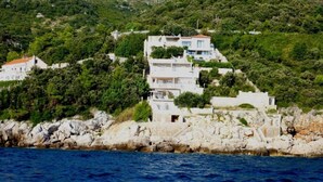 A coastal building with multiple floors, surrounded by greenery and rocky terrain. - 2-bedrooms apartment with AC (Dubrovnik)