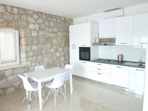 Una cucina moderna con mobili bianchi, una parete in pietra e un'area pranzo con sedie bianche.