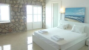 Een slaapkamer met een stenen muur, een bed met witte lakens, een schilderij van een strand en een deur.