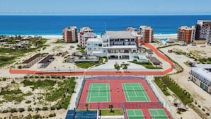 Un hotel costero con varias edificaciones, una cancha de tenis y vista al mar.