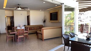 Una sala moderna con un sofá, mesa de comedor, sillas, ventilador de techo y televisor montado en la pared.