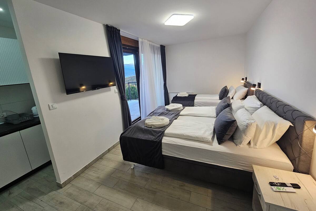 A hotel room with two beds, a TV, a small table, and a view of the outdoors.