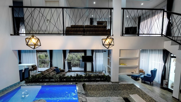 Ampla área interna com piscina, hidromassagem, espaço de relaxamento com sofá e poltronas, e escada que liga dois andares.