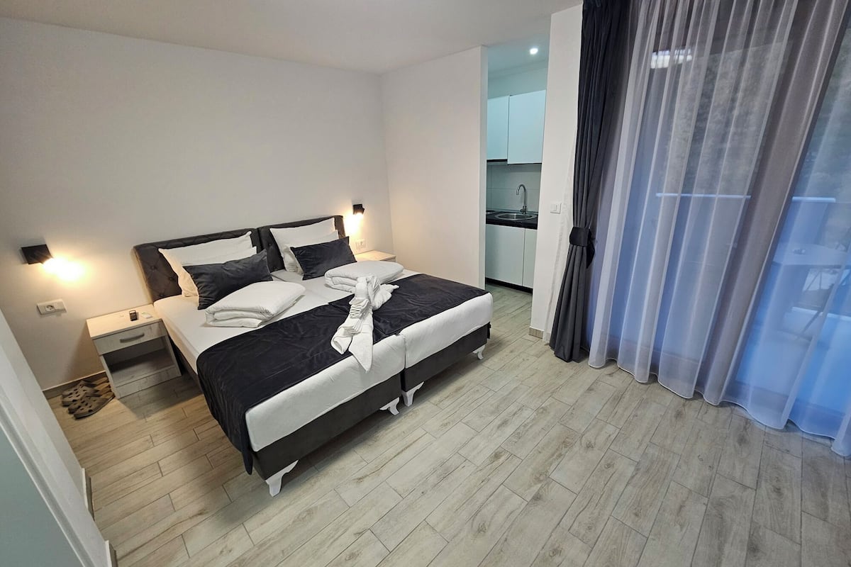 A modern bedroom with a bed, bedside tables, and a view of a kitchen.