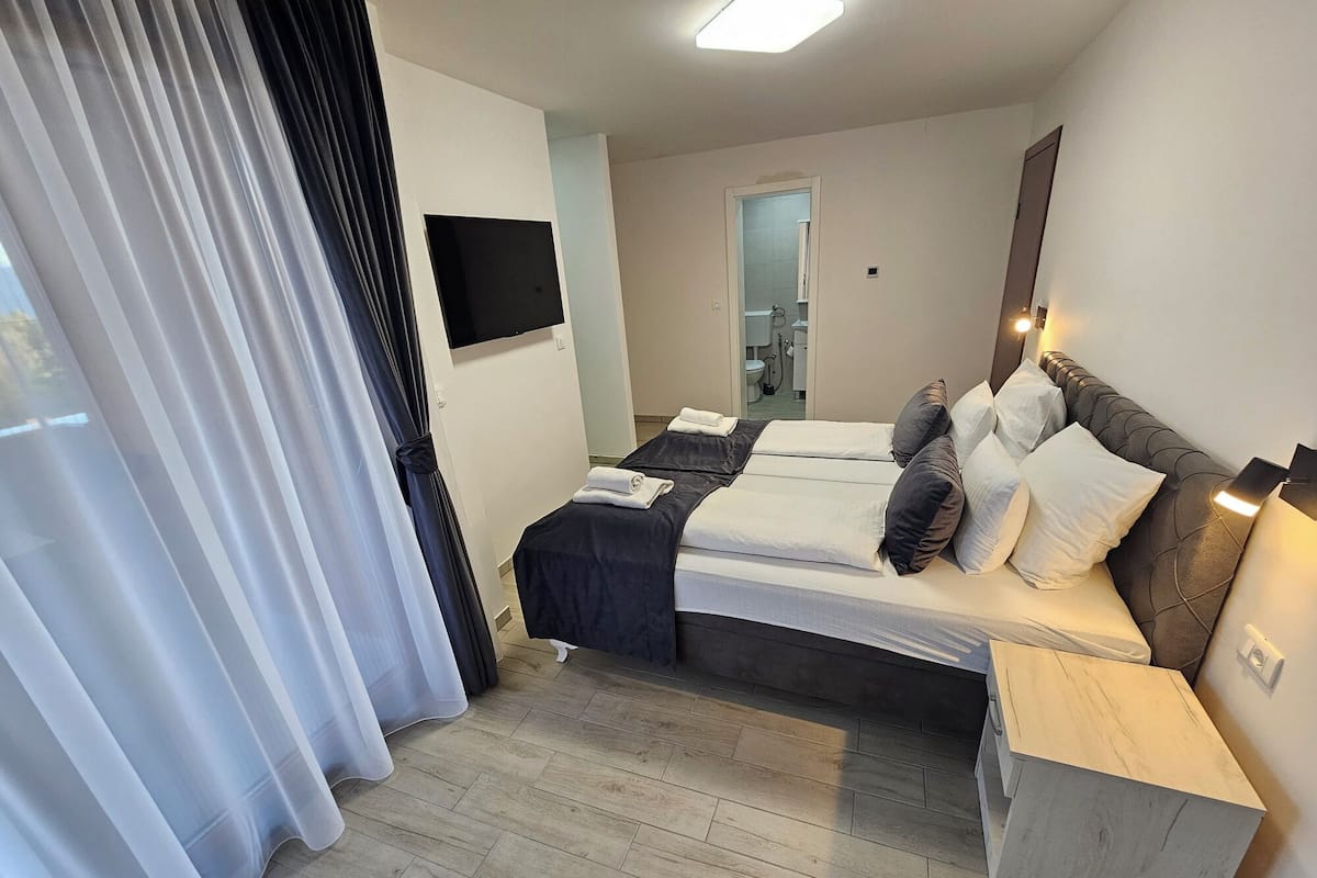 A hotel room with a bed, bedside tables, a TV, and a bathroom visible through an open door.