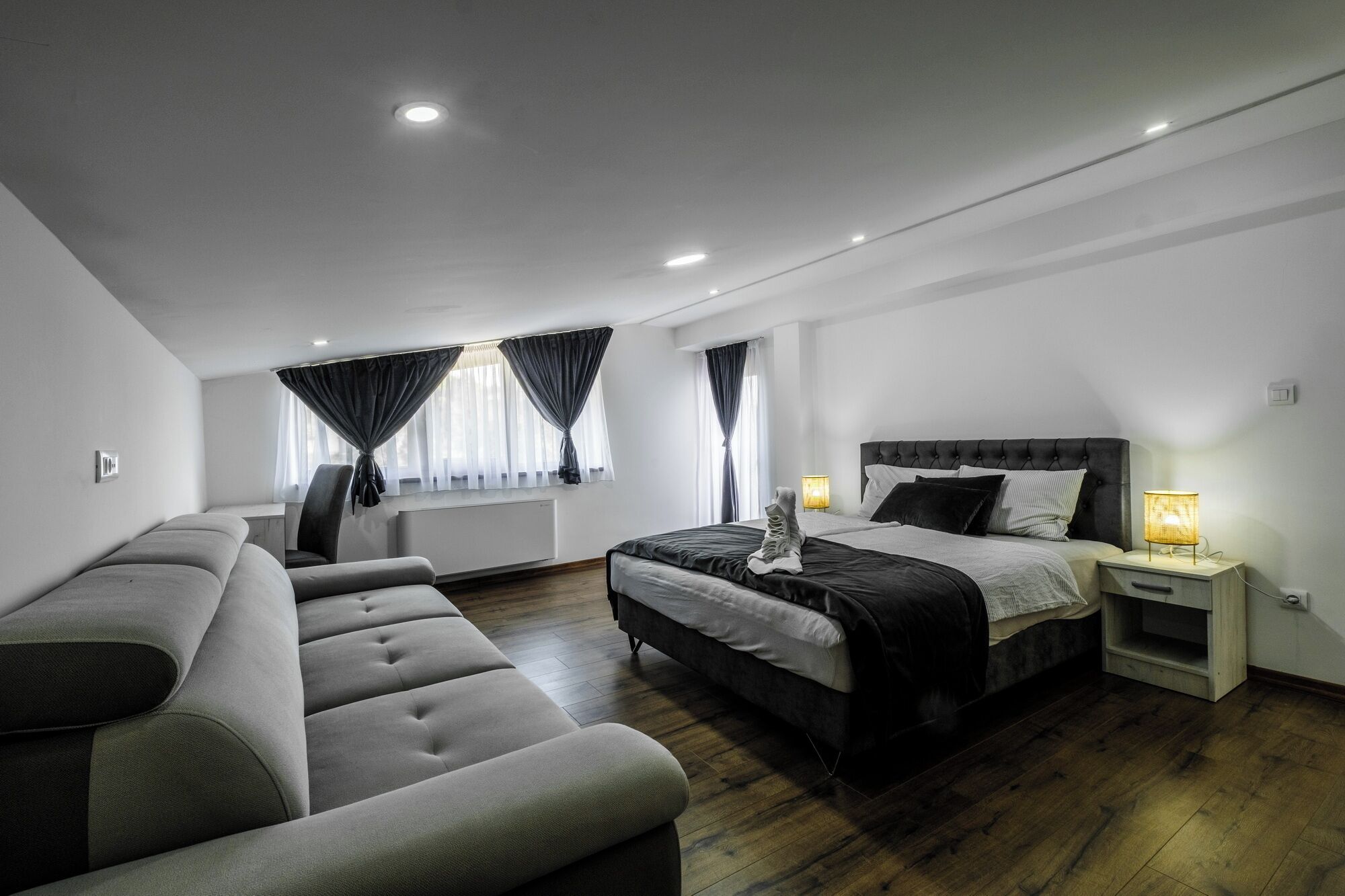Een moderne slaapkamer met een bed, nachtkastjes, een bank en een raam met gordijnen.