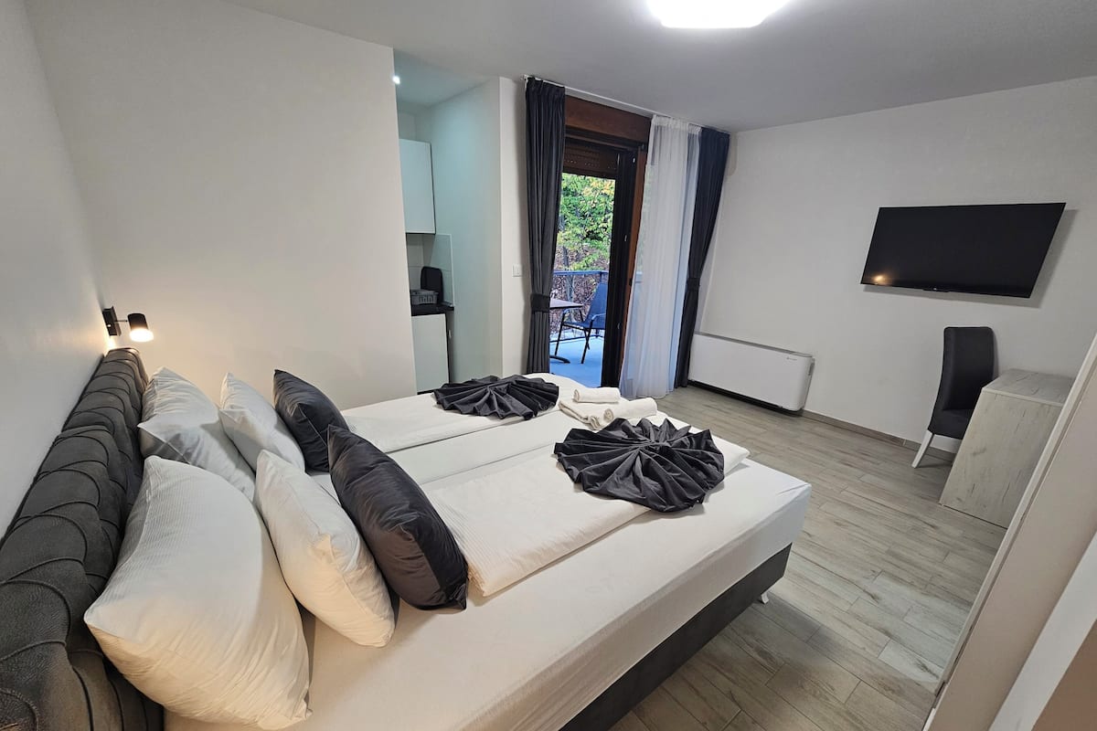 A modern hotel room with a bed, a flat-screen TV, a small table, and a view of the outdoors.