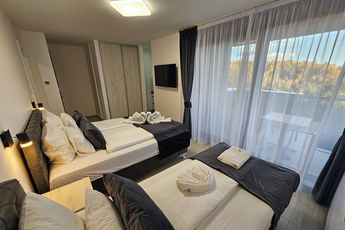 A hotel room with two beds, a TV, a wardrobe, and a balcony with curtains.