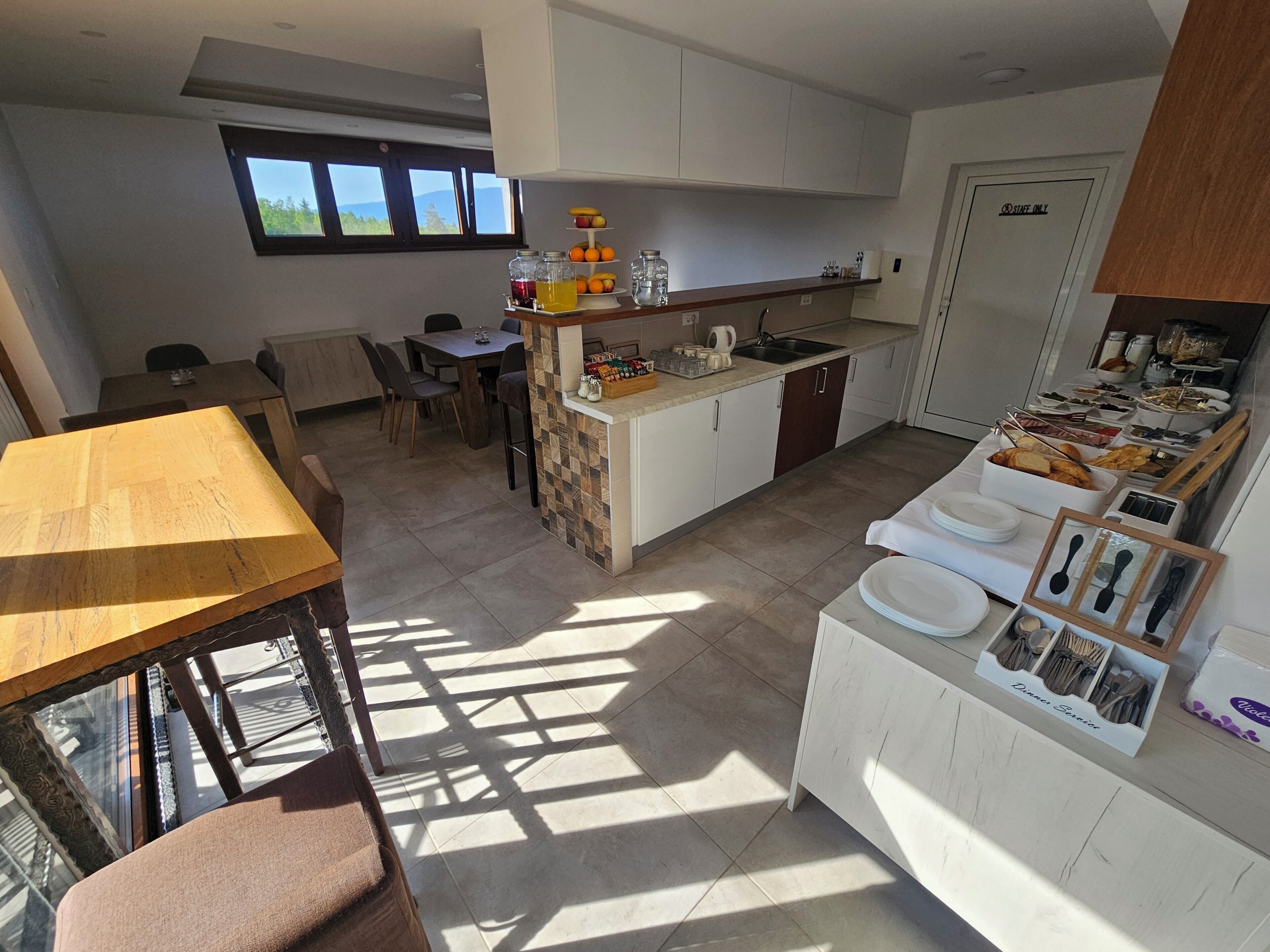 A modern kitchen with a dining area, a window with a view, and a 'STAFF ONLY' door.