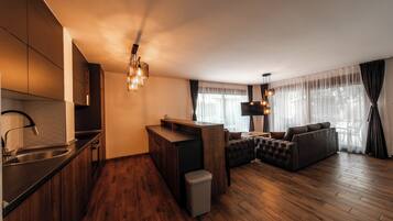 A modern kitchen with a built-in stove, a dining area with a sofa and a TV, and a living room with a large window.