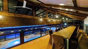 Un restaurante con una larga mesa de madera, sillas y vista a una piscina a través de paredes de vidrio.