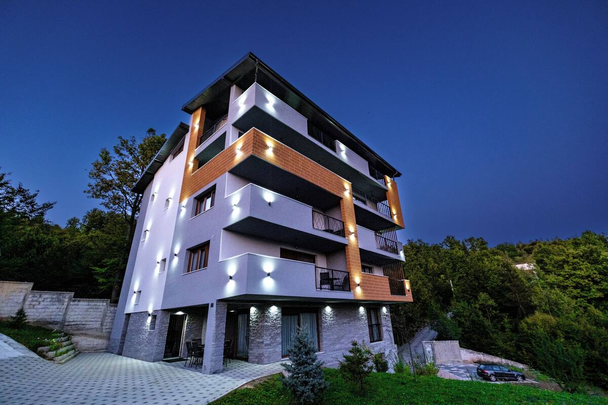 A multi-story residential building with balconies, a paved driveway, and a small garden area.
